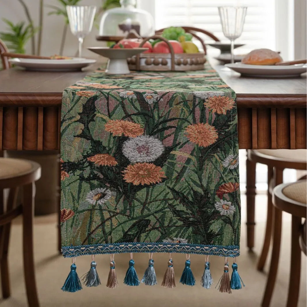 Beige jacquard table runner with floral pattern and long tassel fringes on a table.