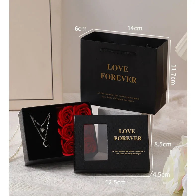 Red Korean-style jewellery gift box open to show six pink soap flowers, with a black handbag beside it.