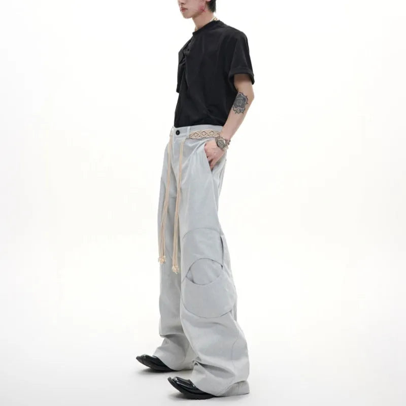 Men's dark blue straight-leg jeans with heavy 3D cutting, belt stitching, and tassel details on a loose fit.