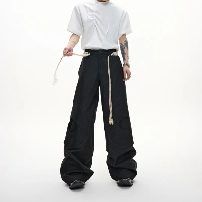 Men's dark blue straight-leg jeans with heavy 3D cutting, belt stitching, and tassel details on a loose fit.