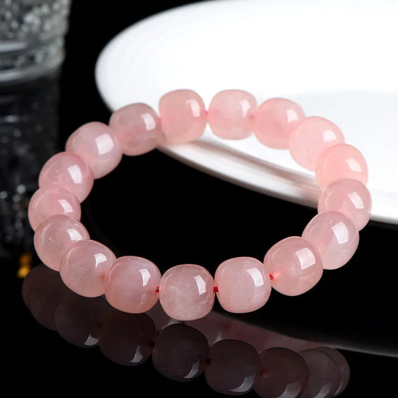Close-up of a pink natural crystal barrel bead bracelet with geometric shaped beads on a wrist.