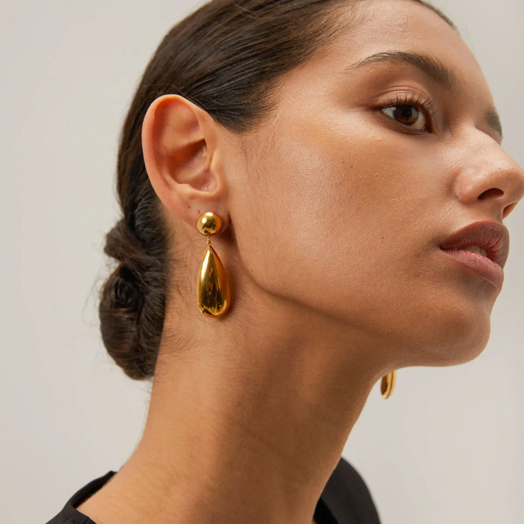 A pair of gold-coloured stainless steel earrings with a geometric water drop and hemisphere pendant design.