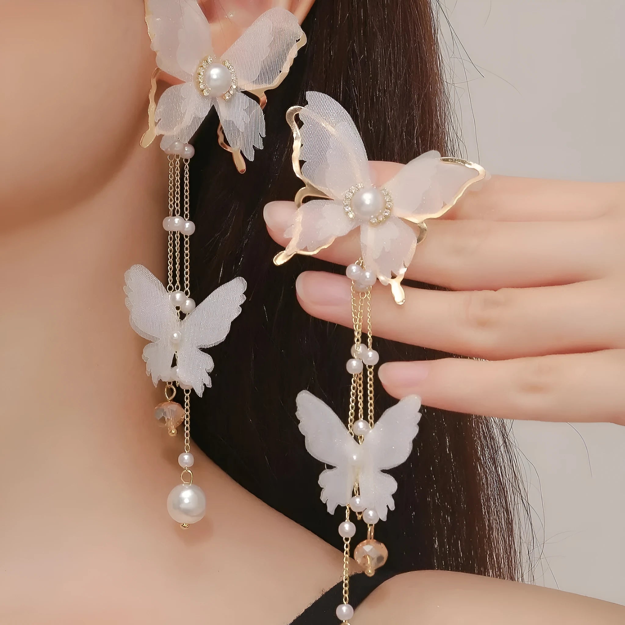 A pair of white butterfly-shaped earrings with pearls, rhinestones, and lace tassels on a copper alloy base.