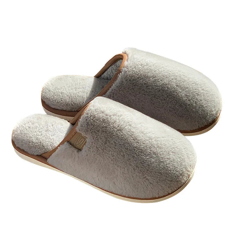 A pair of solid-colour plush winter slippers with a non-slip PVC sole on a wooden floor.