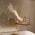 Women's gold stiletto high heel with pointed toe, rhinestone decorations, and a bow.