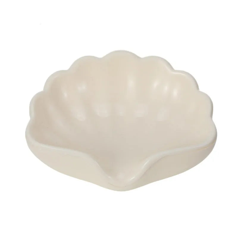 A white or pink plastic shell-shaped soap dish for bathroom counter or shower use.