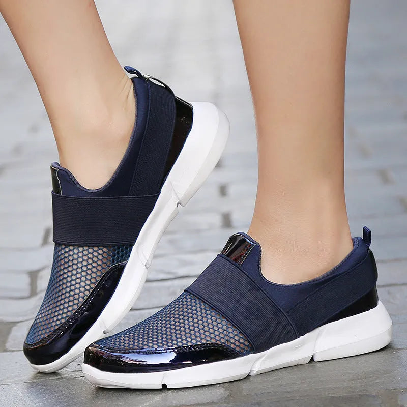 A pair of blue, low-cut women's casual sneakers with a mesh lining on a hard floor surface.