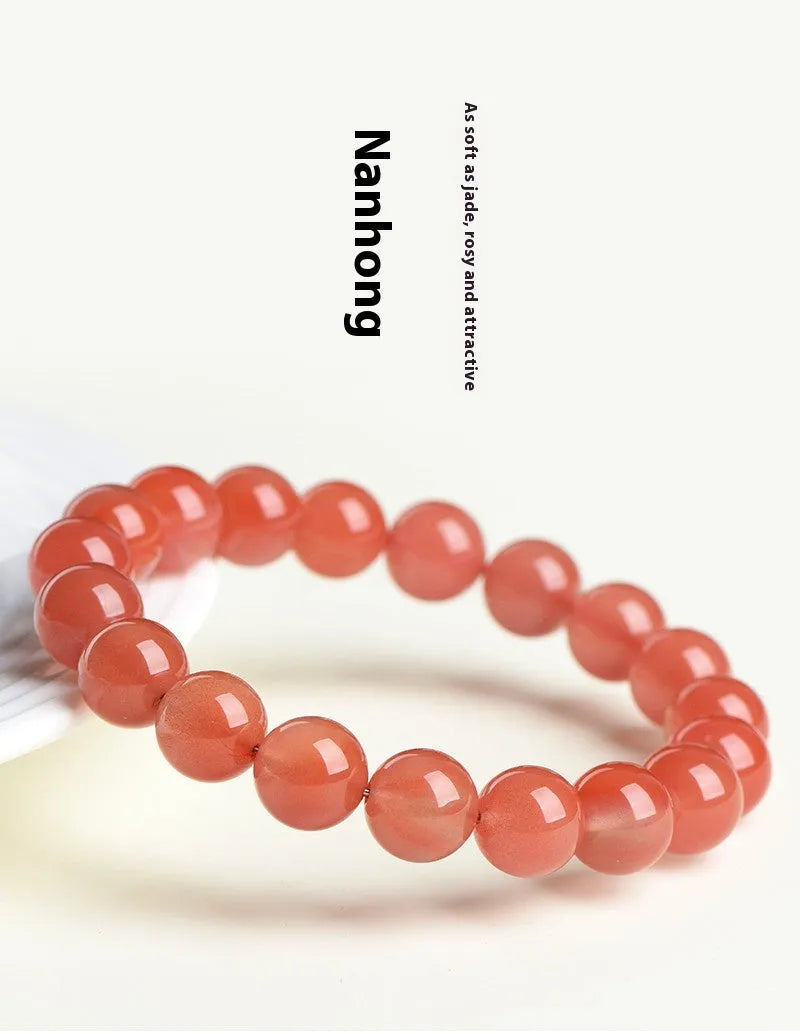 A close-up of a polished cherry red agate bead bracelet on a wrist.