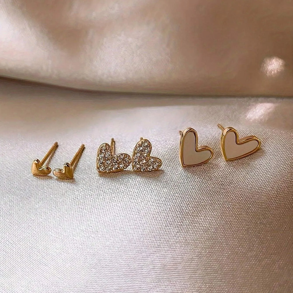Three pairs of heart-shaped alloy earrings in gold, black, black and white, and pink colours on display.
