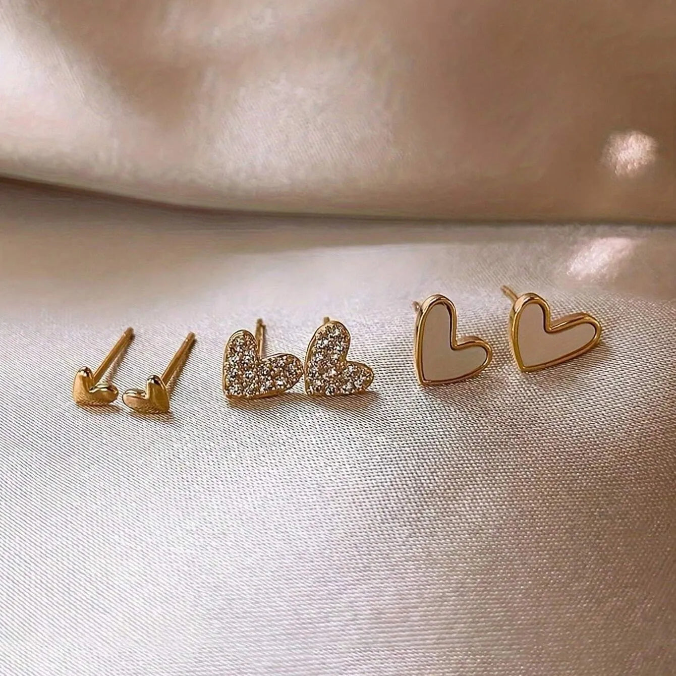 Three pairs of heart-shaped alloy earrings in gold, black, black and white, and pink colours on display.