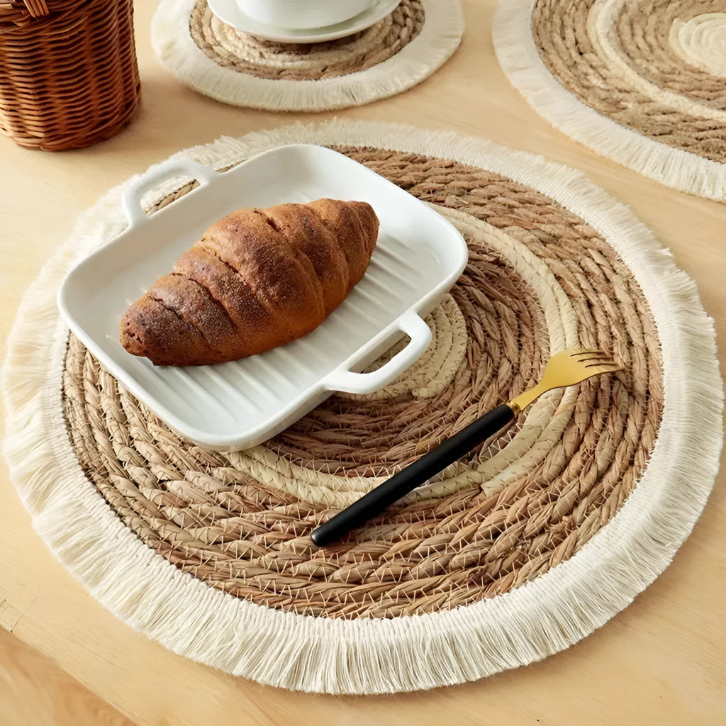Round natural papyrus placemat on a wooden table, showing corn rope tassel detail and modern minimalist style.