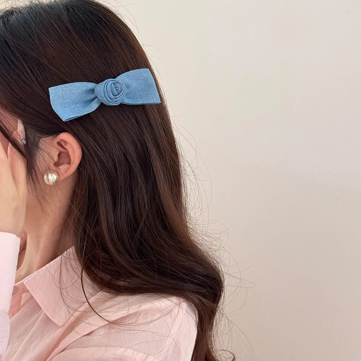 A women's hair clip barrette with a soft blue cloth bow and lace decoration on a plastic clip.