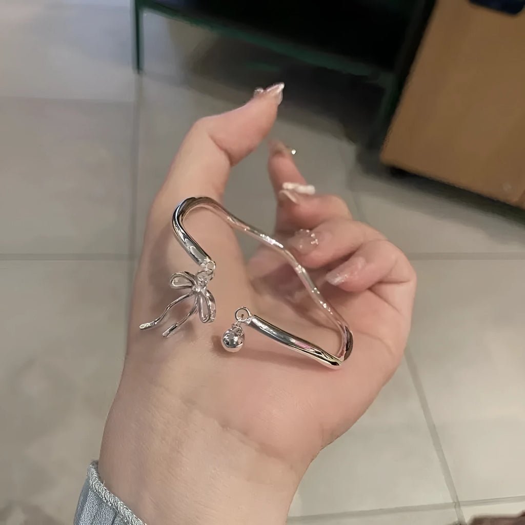 Silver adjustable bracelet with a bow charm on a wrist, showing the bell opening mechanism.