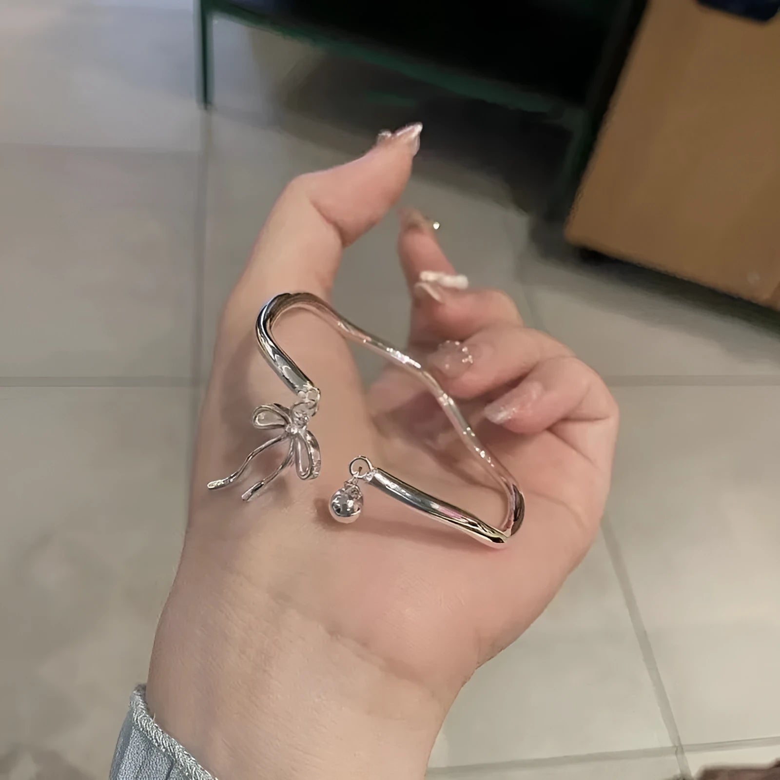 Silver adjustable bracelet with a bow charm on a wrist, showing the bell opening mechanism.