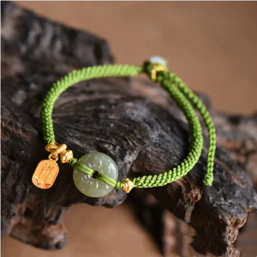 Close-up of a women's hand-woven green rope bracelet with a Hetian jade peace buckle charm.