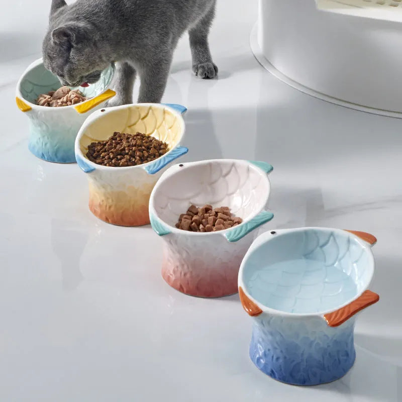 Set of blue fish-shaped ceramic cat bowls with a tilted angle on a wooden surface.