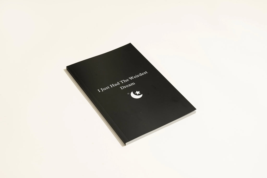 Black hardcover A5 dream journal notebook with lined pages open on a surface.
