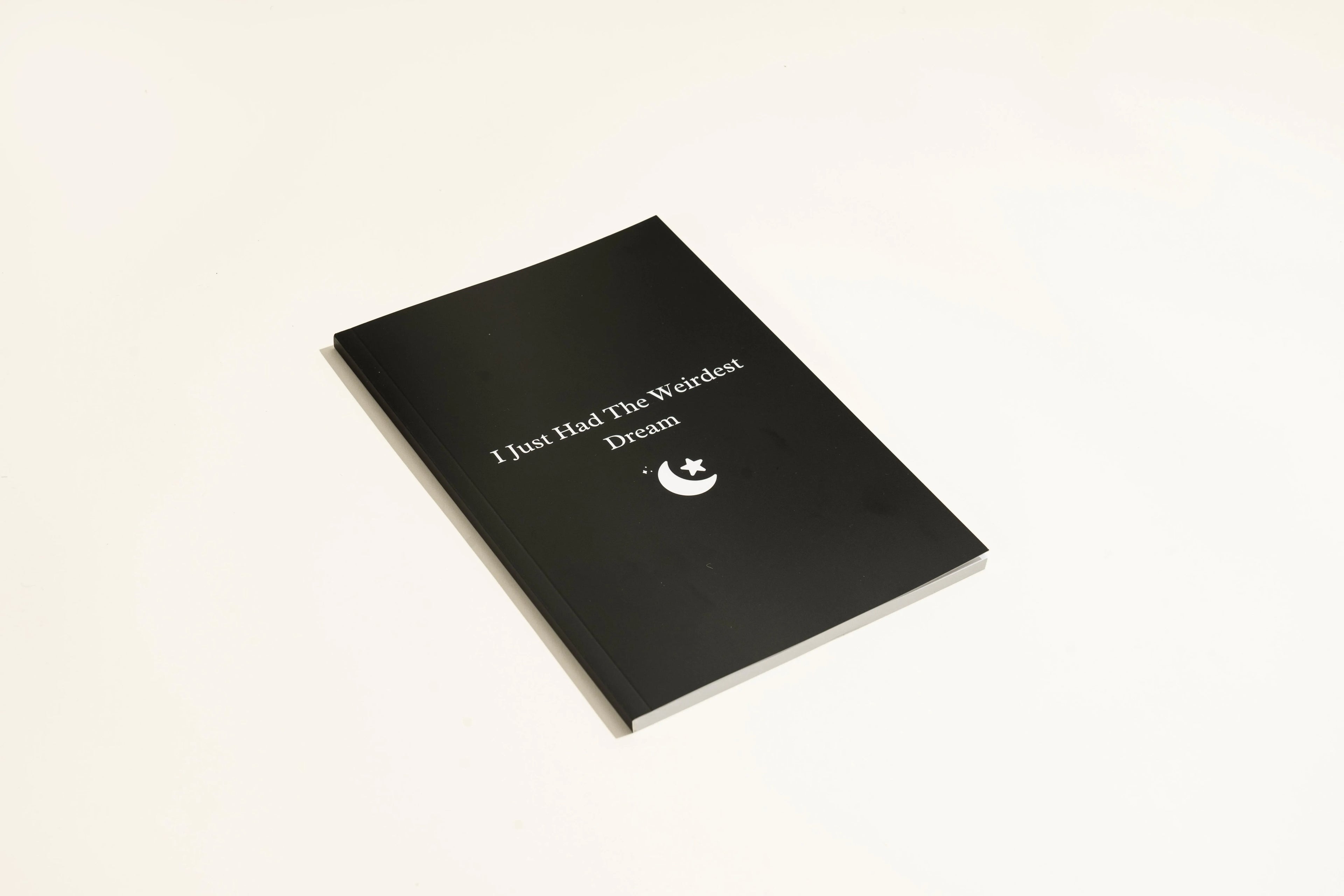 Black hardcover A5 dream journal notebook with lined pages open on a surface.