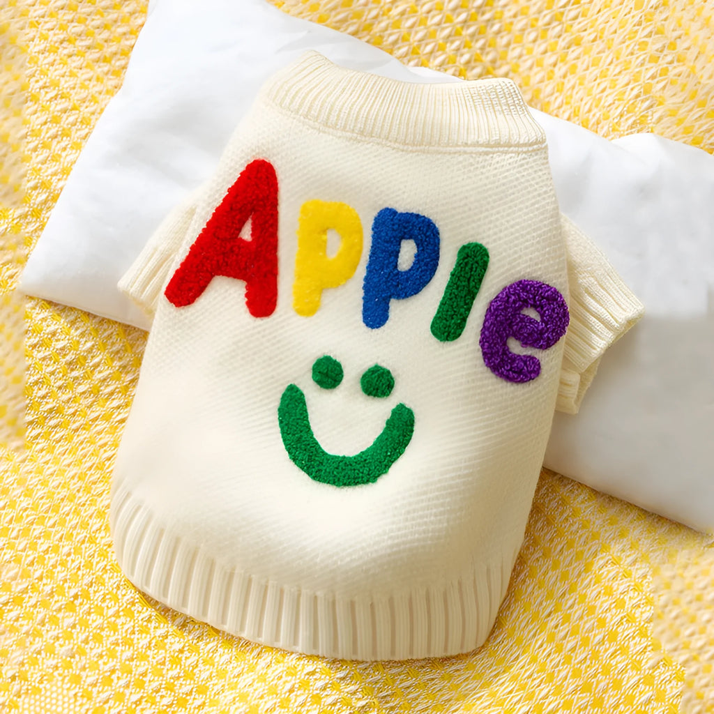 White knitted small dog sweater with rainbow Apple embroidery and green smiley face on a pet