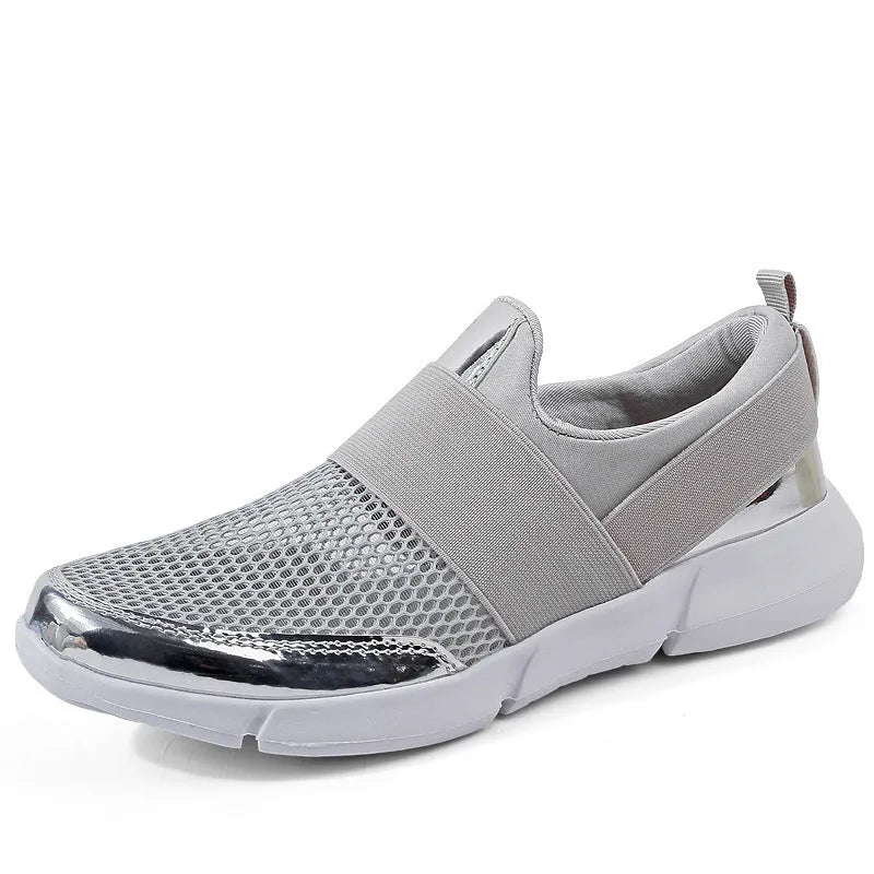 A pair of blue, low-cut women's casual sneakers with a mesh lining on a hard floor surface.