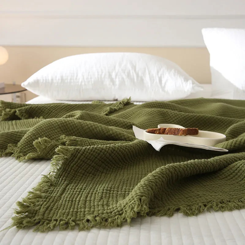 Four-layer gauze cotton blanket with tassel trim in avocado green, laid flat.