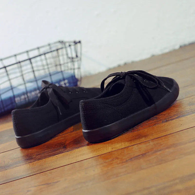 Women's all-black canvas flat lace-up shoes with a slim profile and rubber sole.