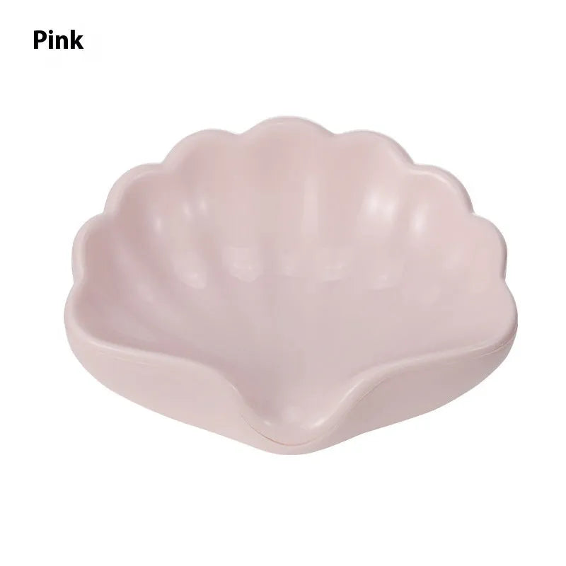 A white or pink plastic shell-shaped soap dish for bathroom counter or shower use.