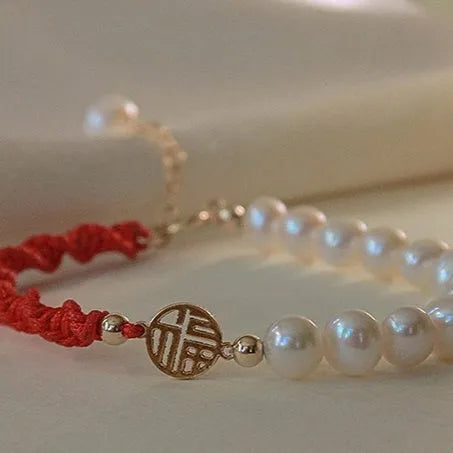 Women's pearl bracelet with gold-plated fu charm on braided red rope