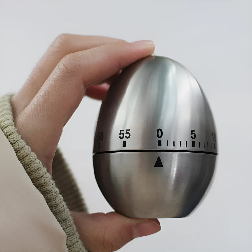 Egg-shaped stainless steel mechanical kitchen timer on a kitchen countertop.