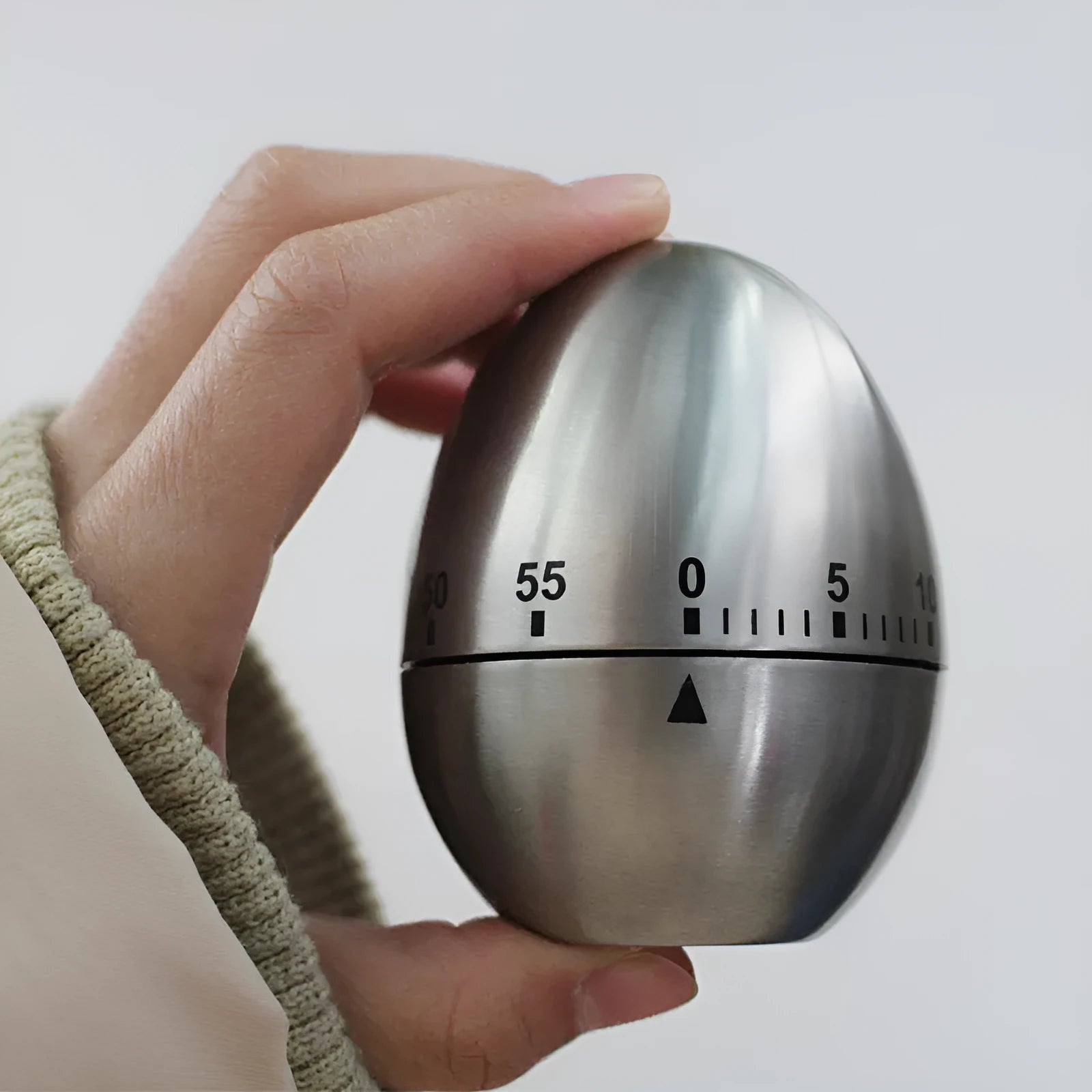 Egg-shaped stainless steel mechanical kitchen timer on a kitchen countertop.