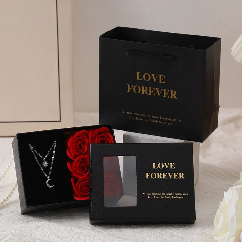 Red Korean-style jewellery gift box open to show six pink soap flowers, with a black handbag beside it.