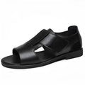 Men's black leather Roman sandals with open toe and non-slip rubber sole on a sandy beach.
