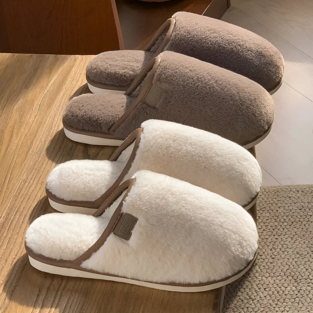A pair of solid-colour plush winter slippers with a non-slip PVC sole on a wooden floor.