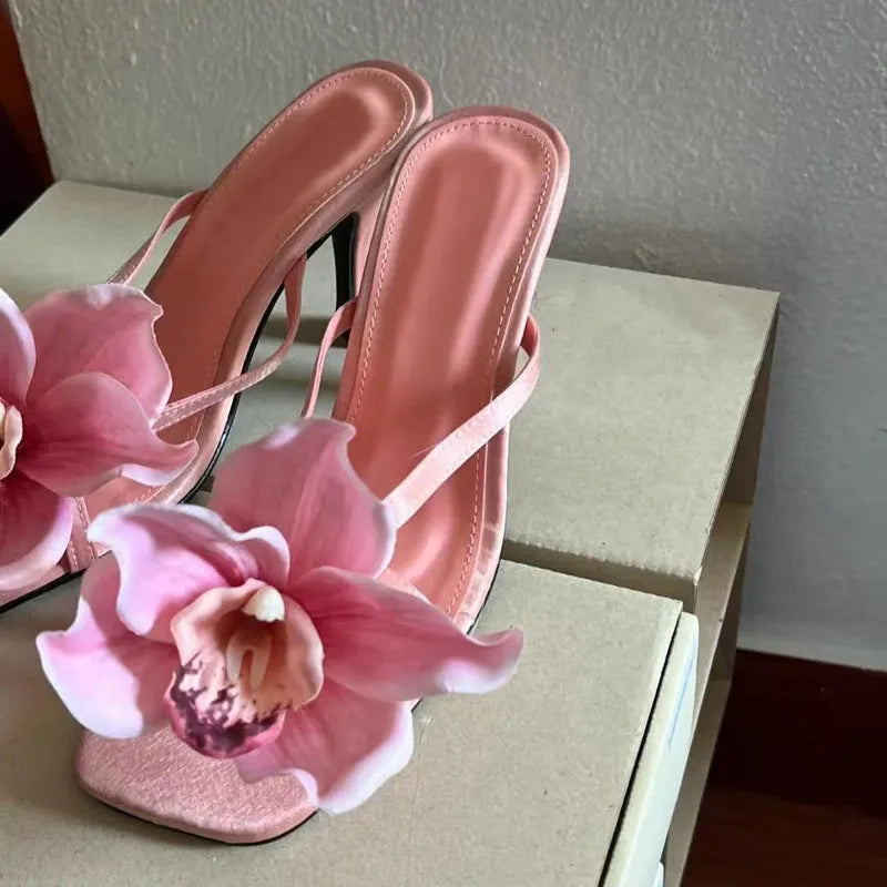Pink women's sandals with artificial Phalaenopsis flower, satin upper, and mid heel.