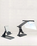 Black detachable mobile phone screen magnifier and holder set up on a desk, showing a phone displaying a magnified movie scene.