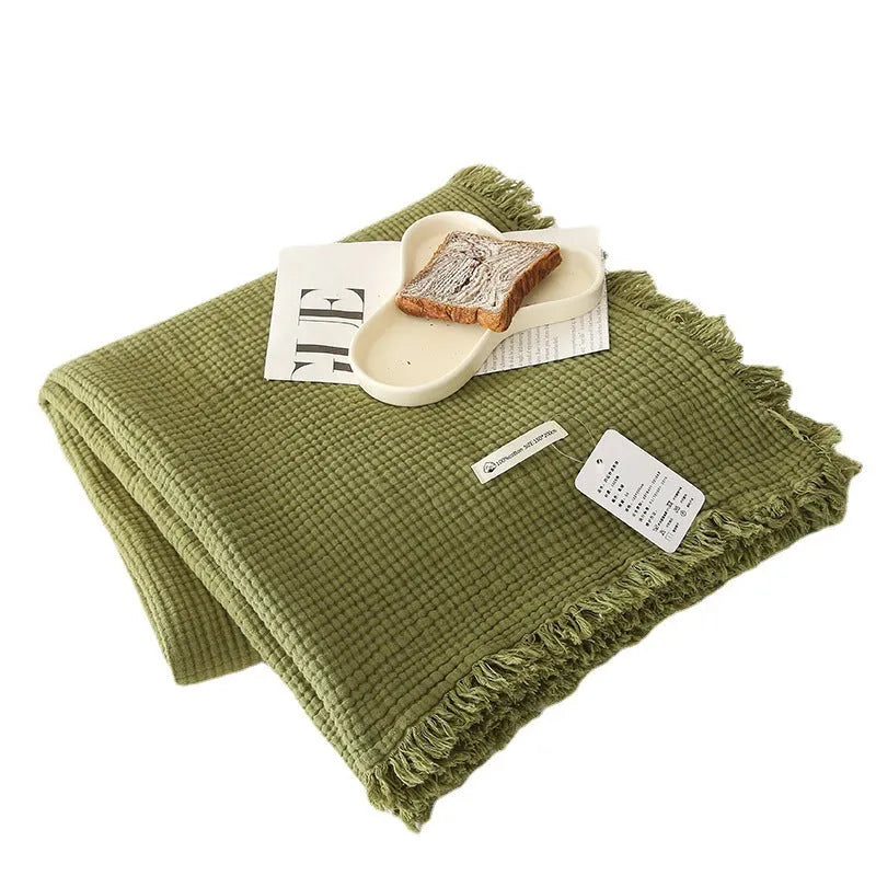 Four-layer gauze cotton blanket with tassel trim in avocado green, laid flat.
