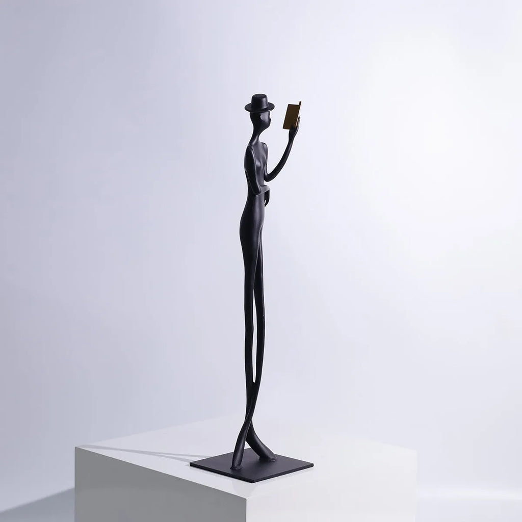 Black minimalist cast aluminum sculpture of a woman reading, 51cm tall on a desktop.