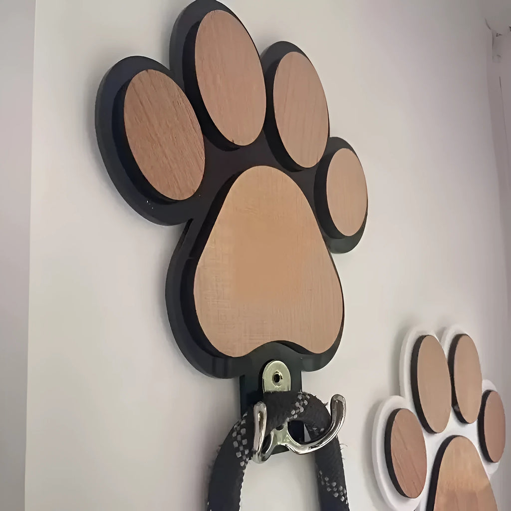 Black wooden wall hook with raised paw print design against a white wall.