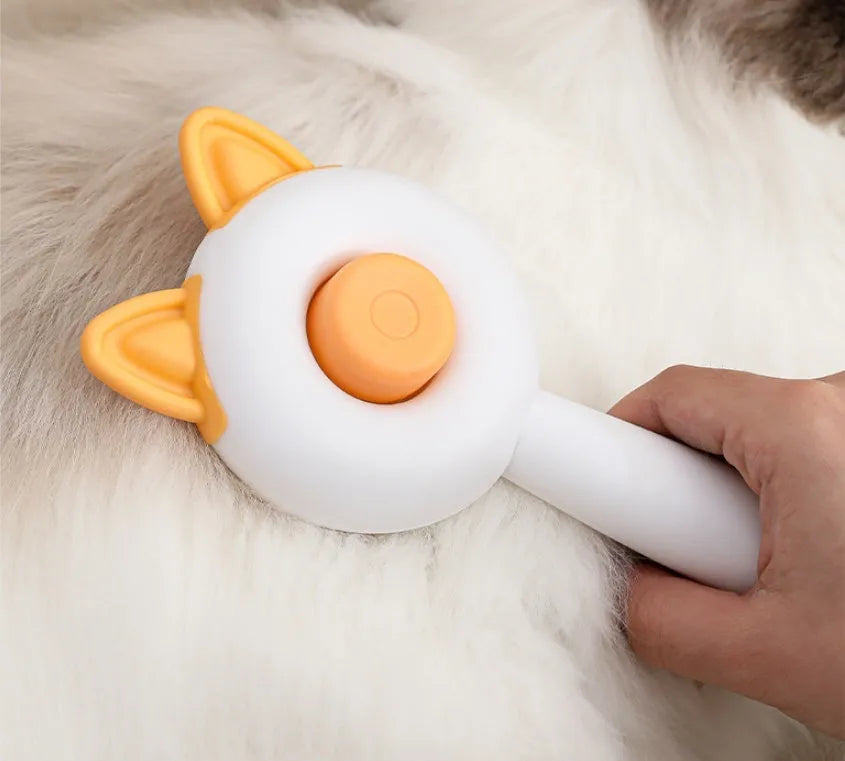 Greenish white cat grooming brush with stainless steel teeth and a self-cleaning button on the handle.