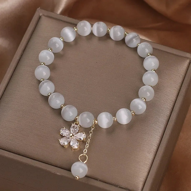 Close-up of a women's single loop bracelet with a white cat's eye stone, flower tassel, and pink morganite safety buckle pendant.