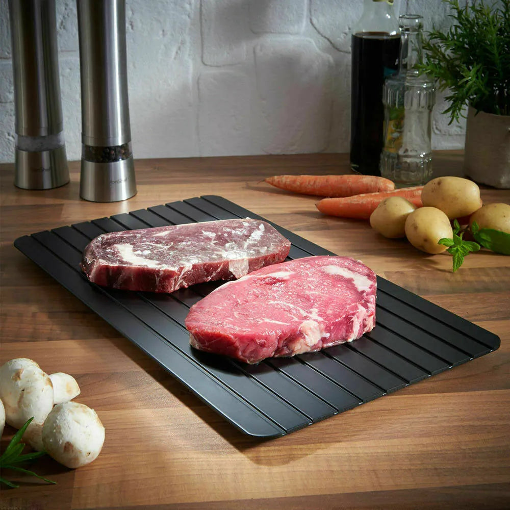 Black rectangular aluminium fast defrost tray for thawing frozen food on a kitchen counter.