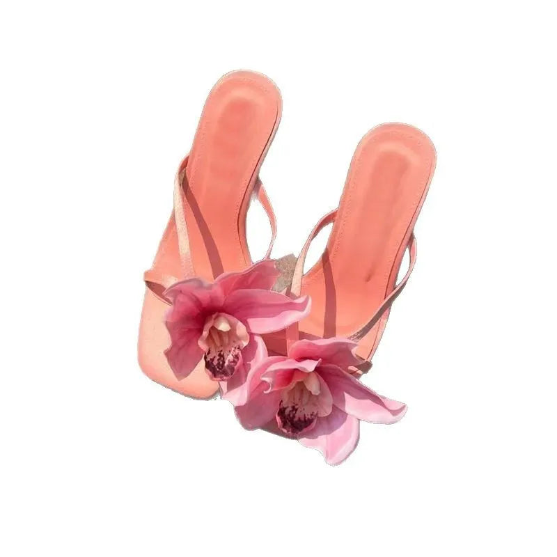 Pink women's sandals with artificial Phalaenopsis flower, satin upper, and mid heel.