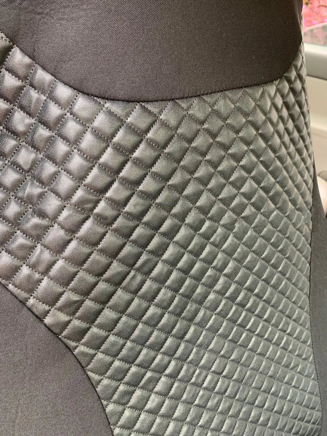 Black quilted automotive seat cover made of PU and polyester fabric, shown with plastic attachment hooks.