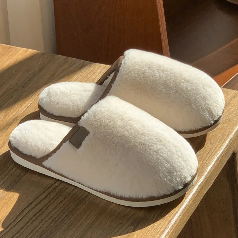 A pair of solid-colour plush winter slippers with a non-slip PVC sole on a wooden floor.