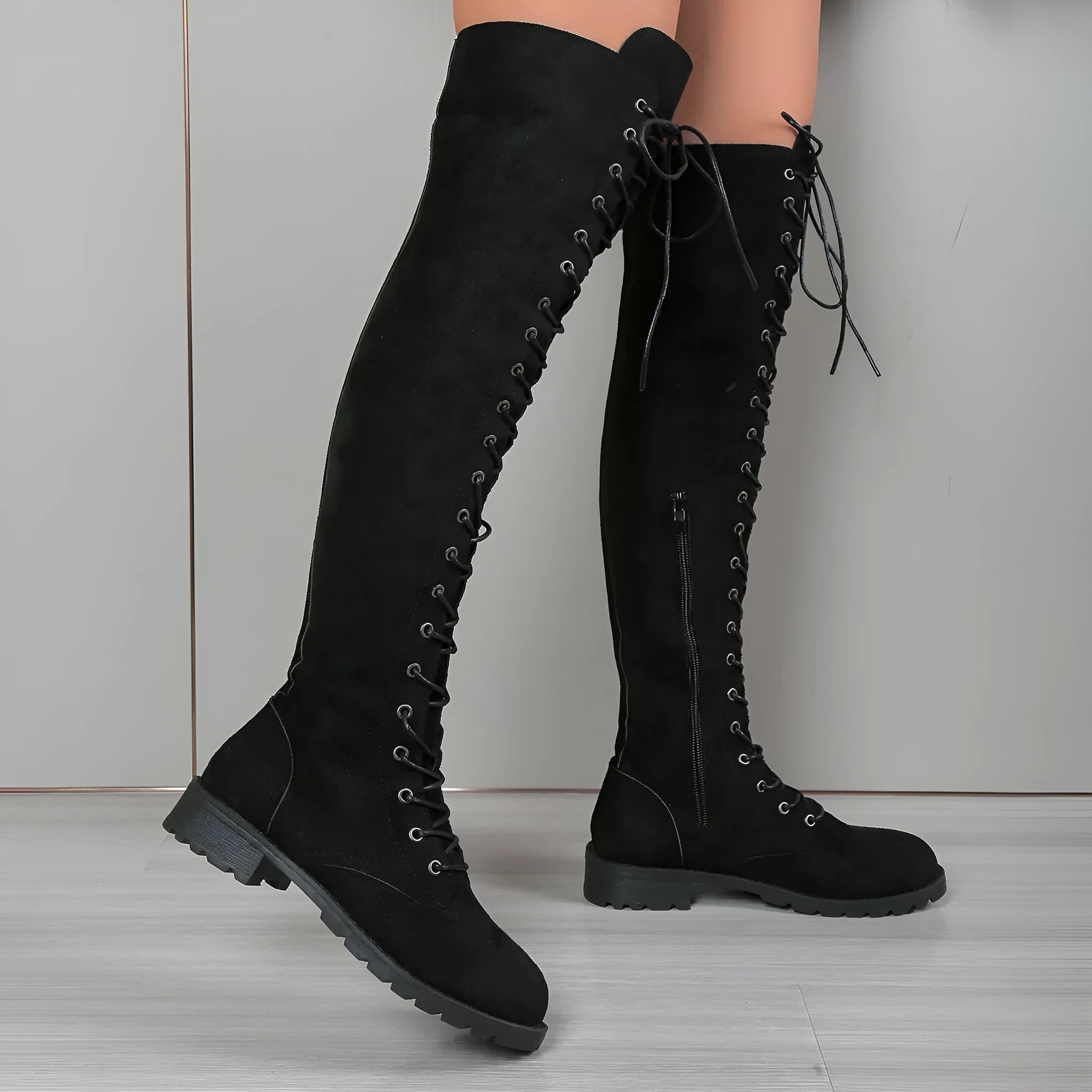 Black lace-up over-the-knee boots with a round head and flat rubber sole on a neutral background.