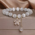 Close-up of a women's single loop bracelet with a white cat's eye stone, flower tassel, and pink morganite safety buckle pendant.