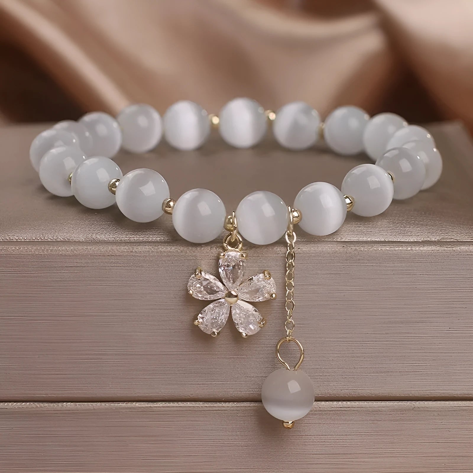 Close-up of a women's single loop bracelet with a white cat's eye stone, flower tassel, and pink morganite safety buckle pendant.