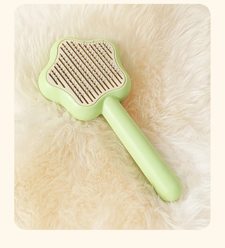 Green and yellow self-cleaning stainless steel cat comb with needle teeth on a wooden table.