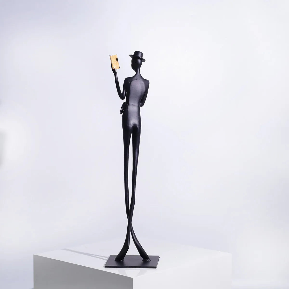 Black minimalist cast aluminum sculpture of a woman reading, 51cm tall on a desktop.