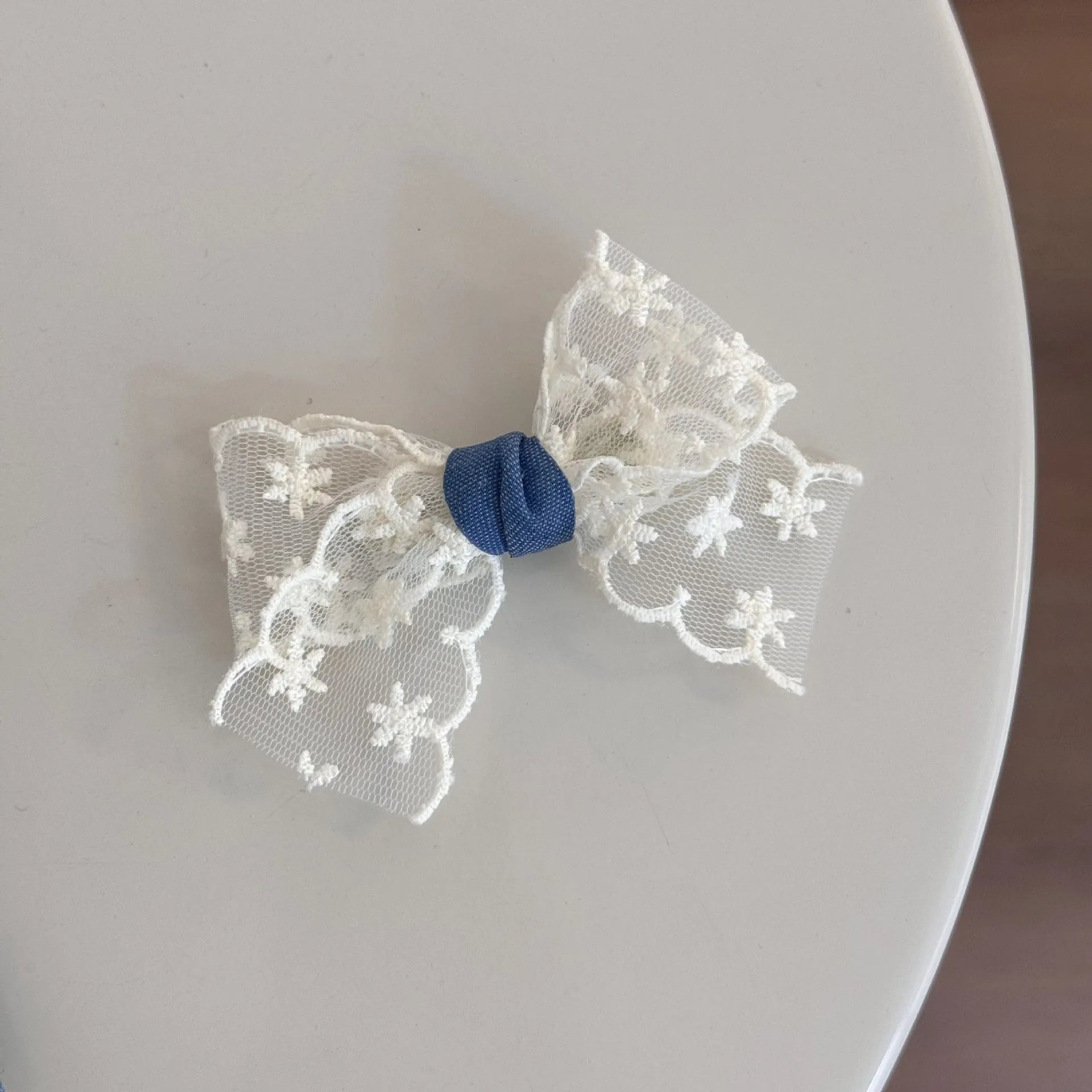 A women's hair clip barrette with a soft blue cloth bow and lace decoration on a plastic clip.